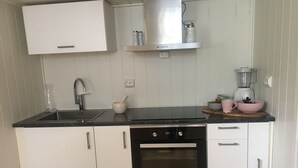 A modern kitchen with white cabinets, a black countertop, a built-in oven, and a stainless steel range hood. - Otra Inn (Vennesla)