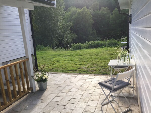 A patio with a table and chairs, a potted plant, and a view of a grassy area.