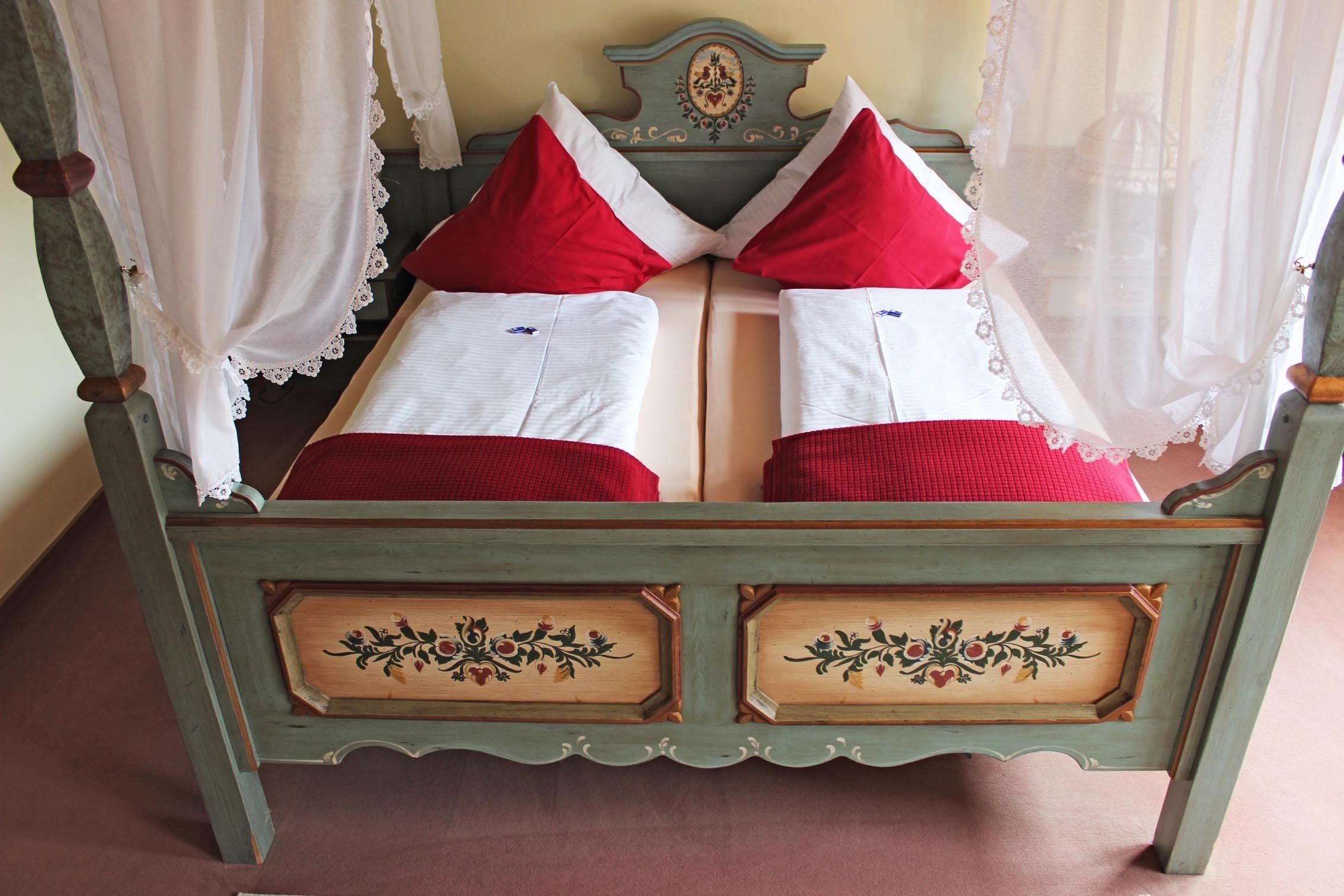 A bed with a green frame, white linens, and red pillows.