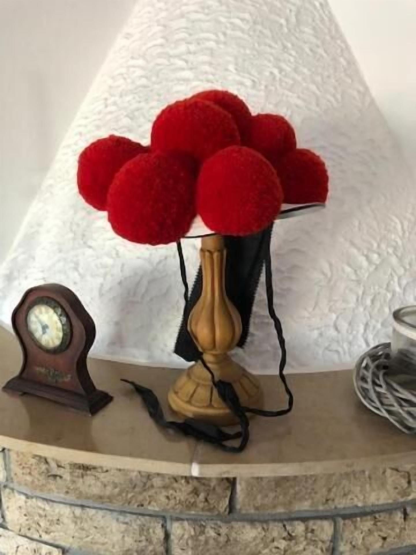 Une horloge, un vase orné de pompons rouges et un chandelier posés sur un mur de pierre.