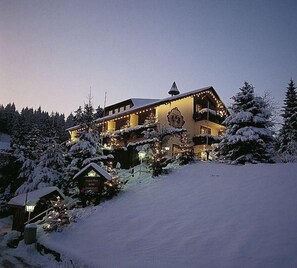 A snow-covered lodge with multiple balconies and a prominent roof structure, surrounded by snow-laden trees. - Hotel Adlerschanze (Schoenwald)