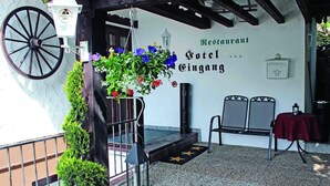 Hotellin sisäänkäynti, jossa on kukka-asetelma, kyltti, jossa lukee ”Restaurant Hotel Gingang”, ja ulkona penkki.