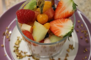 Un tazón de vidrio transparente lleno de frutas variadas sobre un plato.