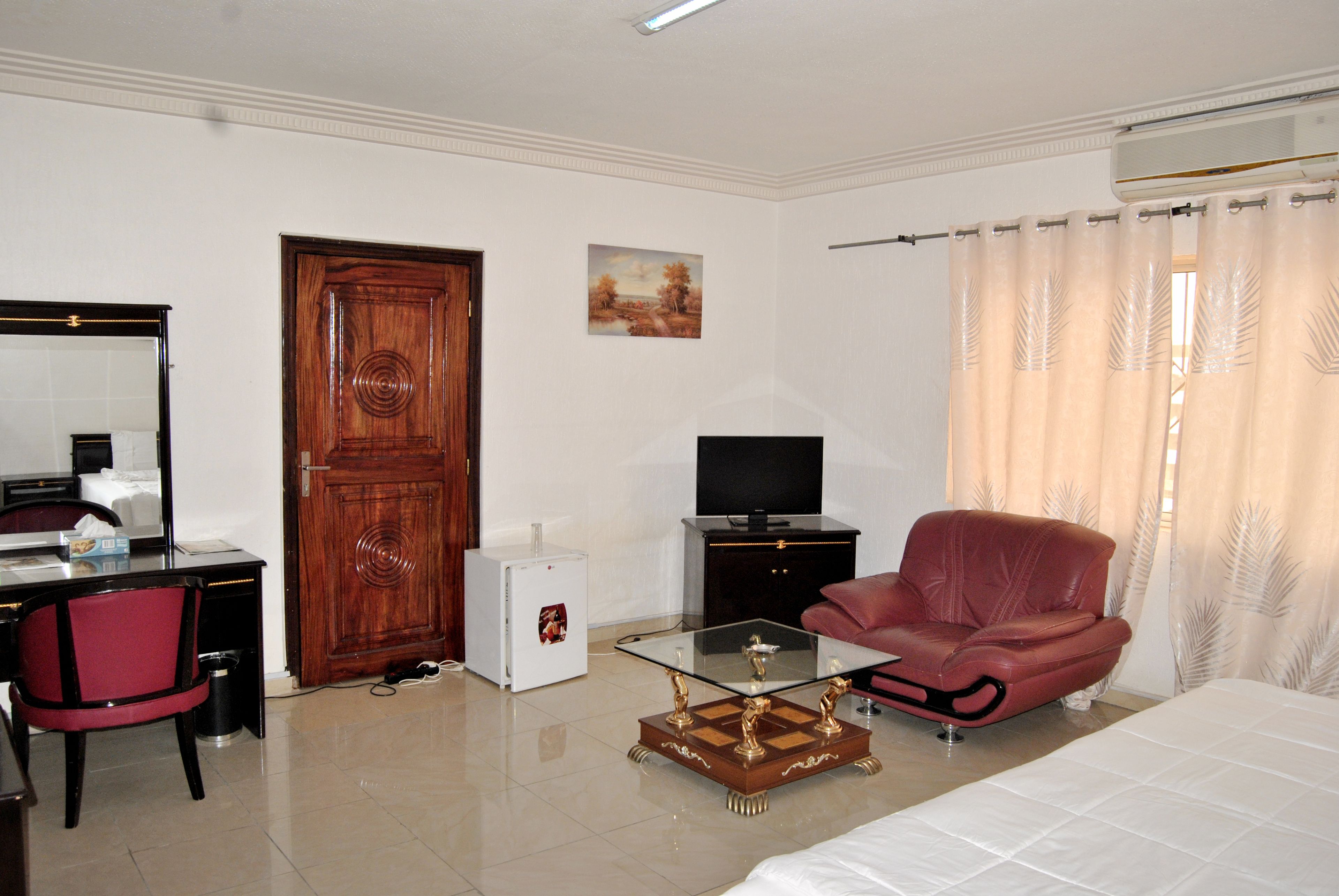 Une chambre d’hôtel avec un lit, un bureau équipé d’un ordinateur, une télévision, une chaise rouge et un petit réfrigérateur.