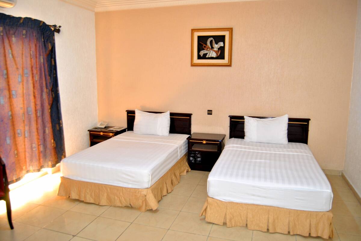 A hotel room with two beds, a nightstand, a dresser, and a framed picture on the wall.