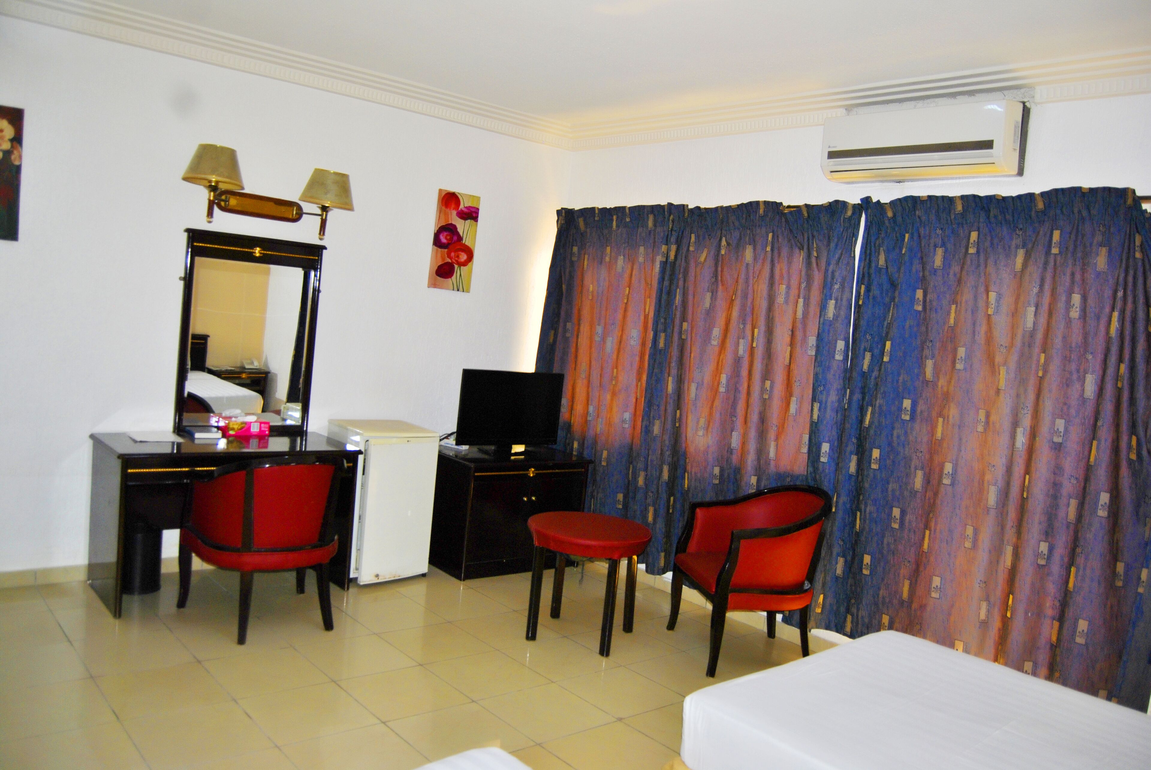 A hotel room with a desk, two red chairs, a bed, a television, and a curtain.