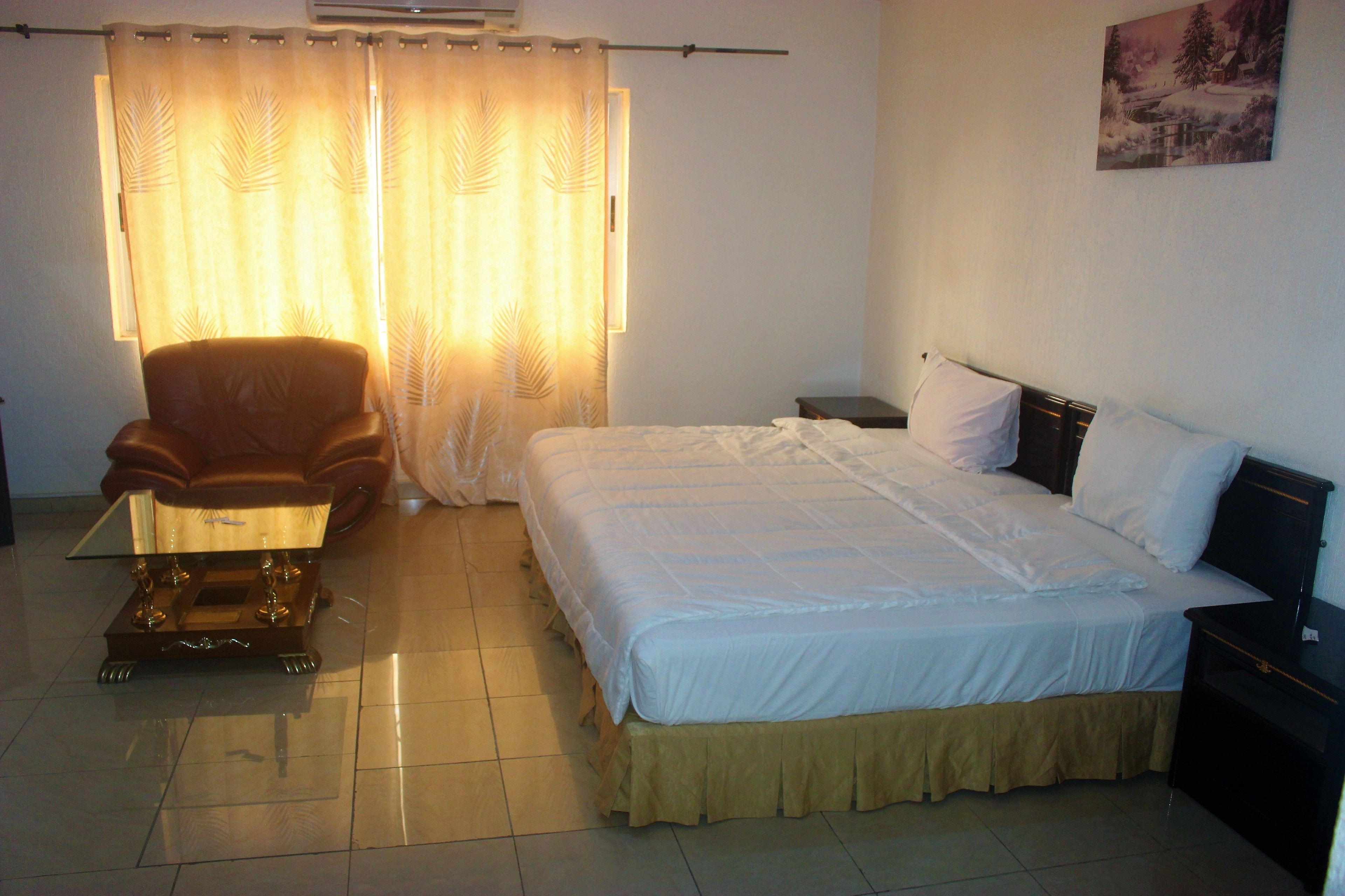 A hotel room with a bed, a chair, a nightstand, and a wall-mounted picture.