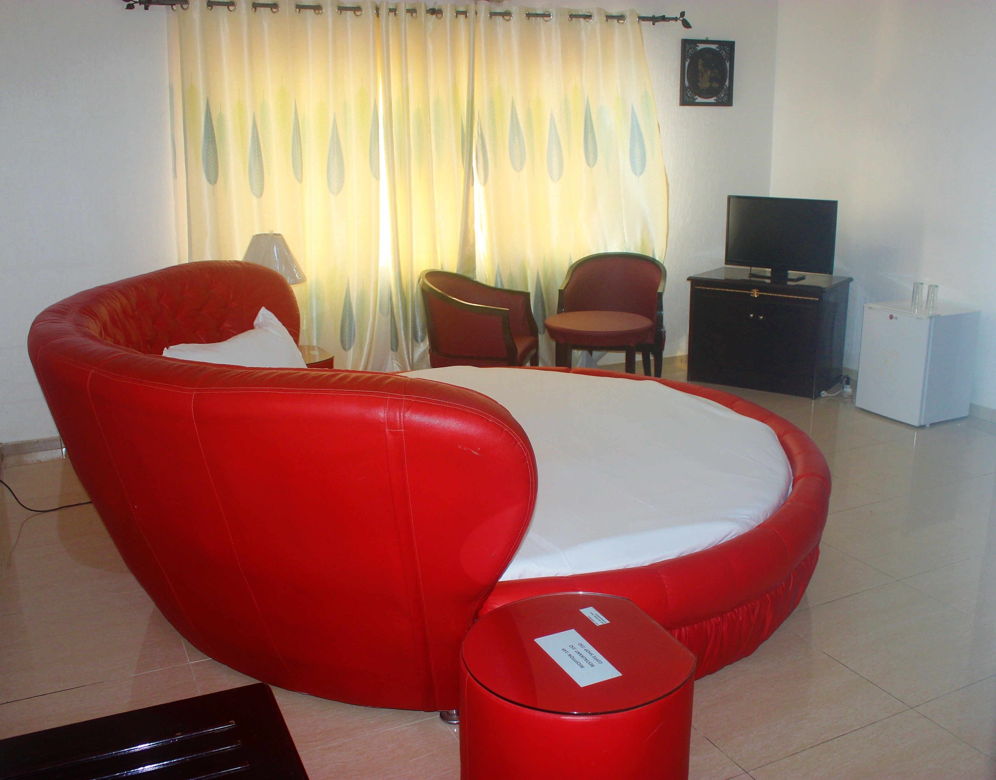 Habitación roja con cama individual, una mesita, una silla, televisor y refrigerador.