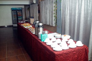 A buffet setup with a red tablecloth, plates, bowls, and a coffee maker.