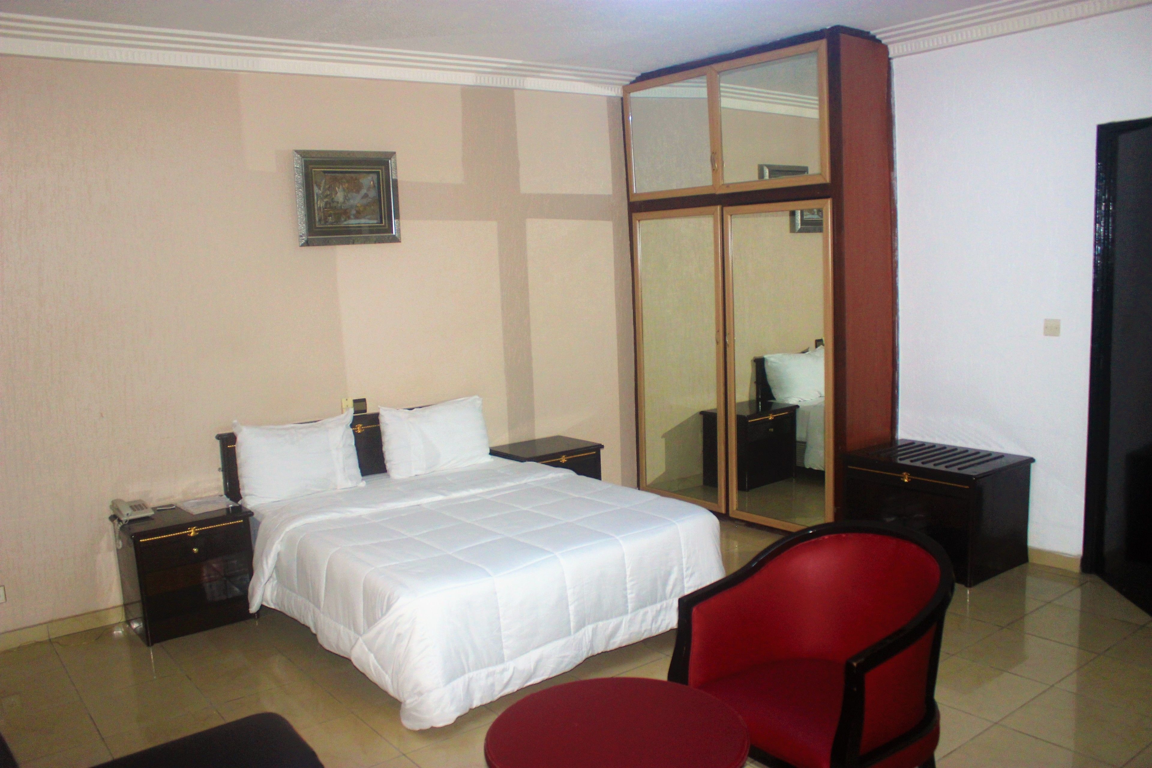 Ein Hotelzimmer mit einem Bett, Nachttischen, einem roten Sessel, einem kleinen Tisch und einem Spiegel.