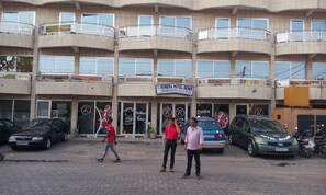 A multi-story hotel with balconies, a signboard, and parked cars.