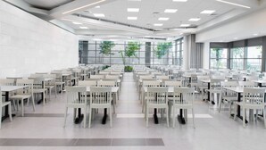 A spacious, modern dining area with rows of white tables and chairs, large windows, and a clean, minimalist design. - HI  Haifa Hostel (Haifa)