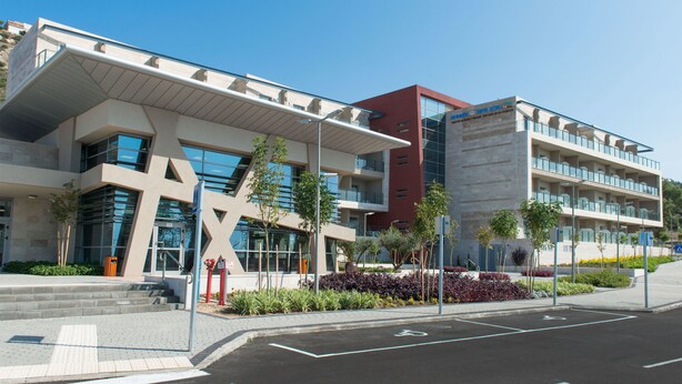 A modern building with a unique architectural design, featuring a prominent cross-like structure and multiple balconies. - HI  Haifa Hostel (Haifa)