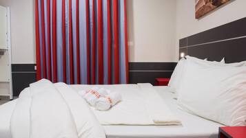 Una habitación de hotel con una cama bien hecha, una mesita de noche roja y una cortina a rayas.