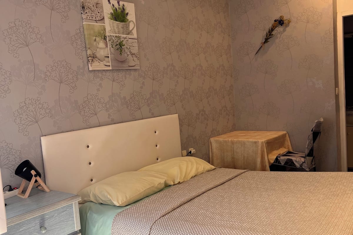 A bedroom with a bed, nightstand, dresser, and a small table with a lamp.