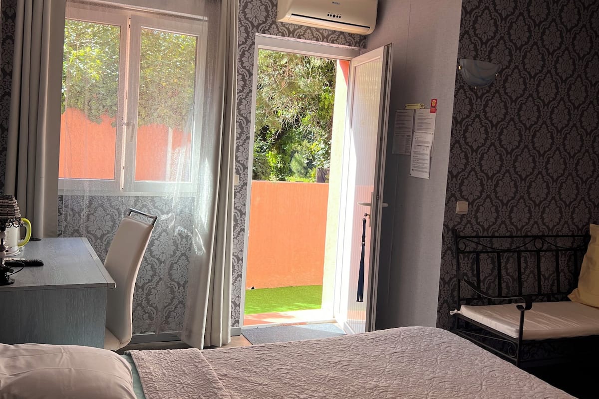 A hotel room with a bed, a desk with a chair, an air conditioning unit, and a view of the outside.