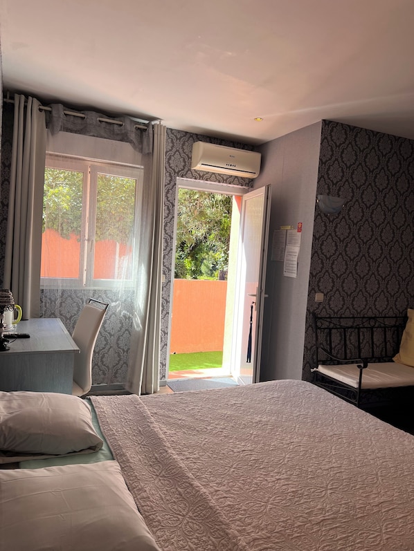 A hotel room with a bed, a desk with a chair, an air conditioning unit, and a view of the outside.
