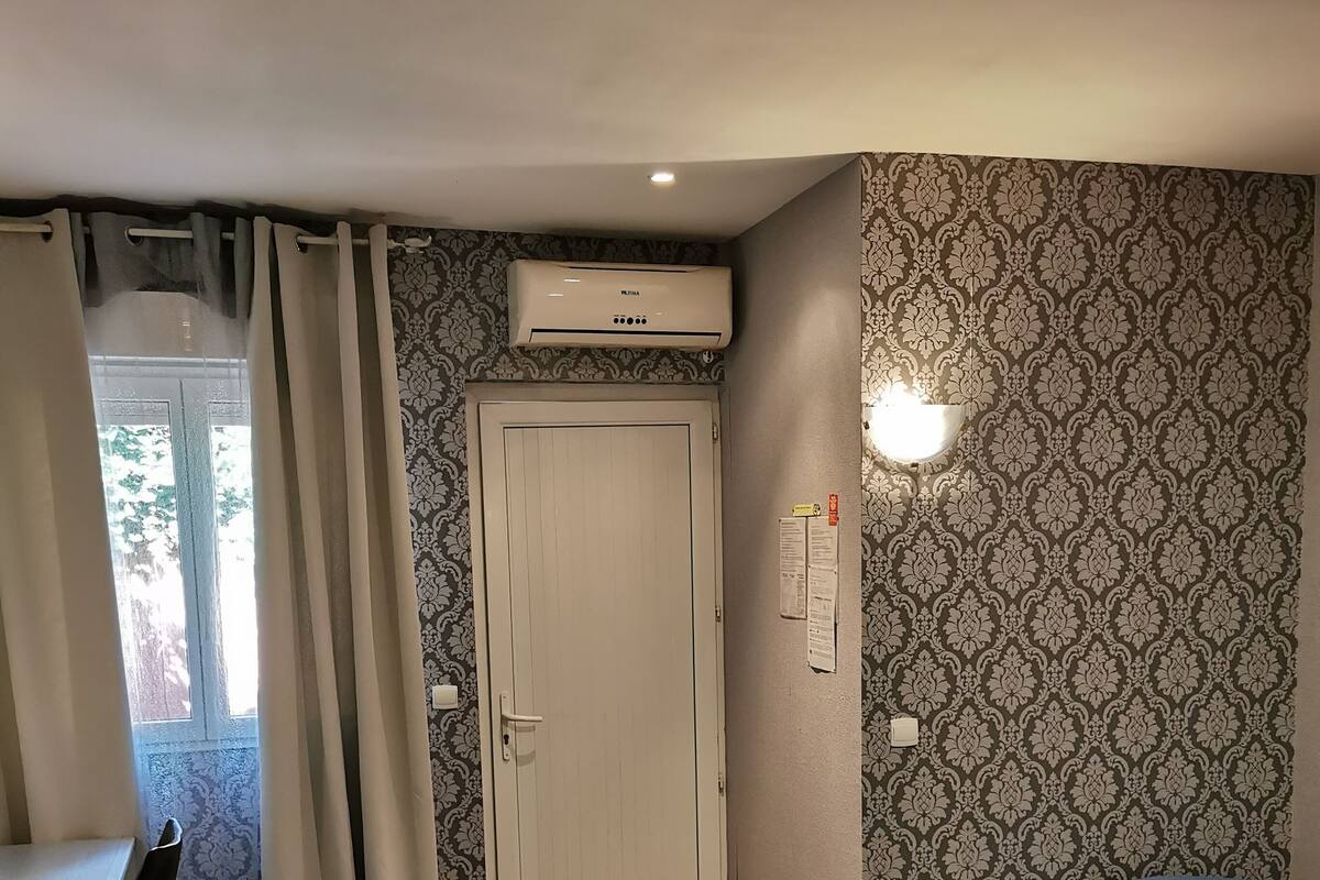A hotel room with two beds, a desk, an air conditioner, and a patterned wall.