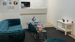 A modern living room with a teal sofa, a round ottoman, a glass coffee table, and a white side table with red candles. - Hotel Galeón Boutique (Calpe)