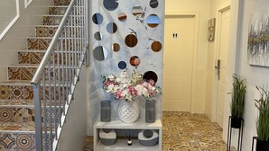 A staircase with patterned tiles, a wall with circular mirrors and a bird mural, and a console table with vases and flowers. - Hotel Galeón Boutique (Calpe)