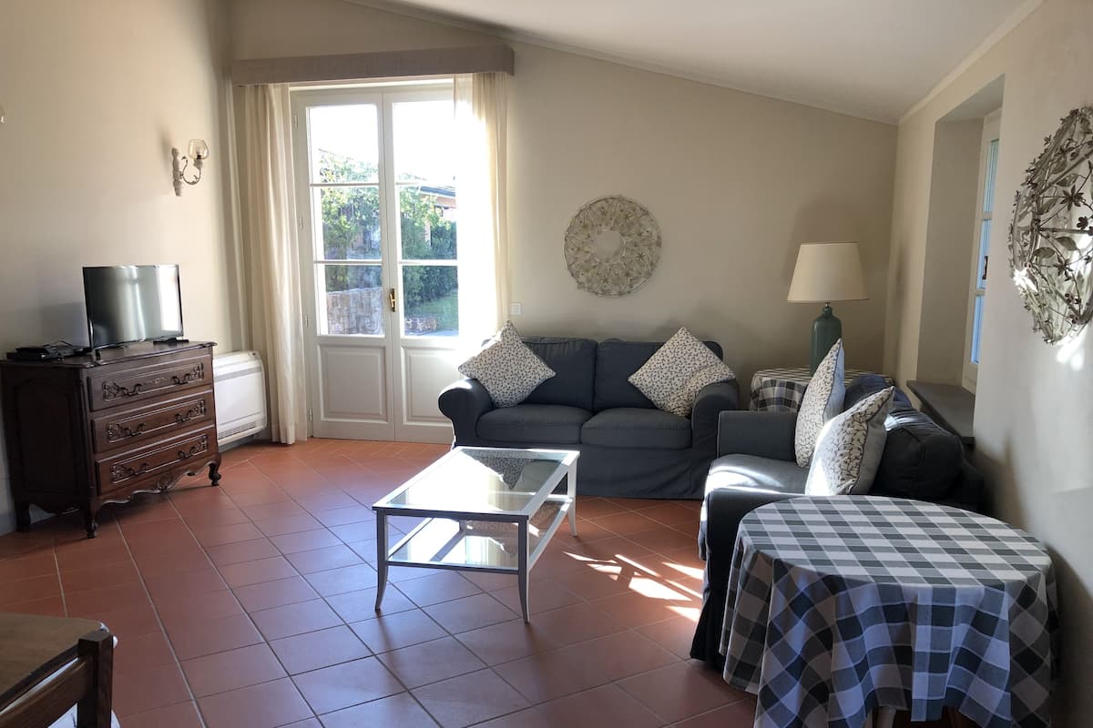 Een woonkamer met een bank, een salontafel, een tv op een dressoir en een raam met gordijnen.