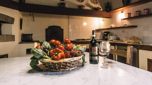 A kitchen with a marble countertop, a basket of fresh vegetables, a bottle of wine, and a glass.