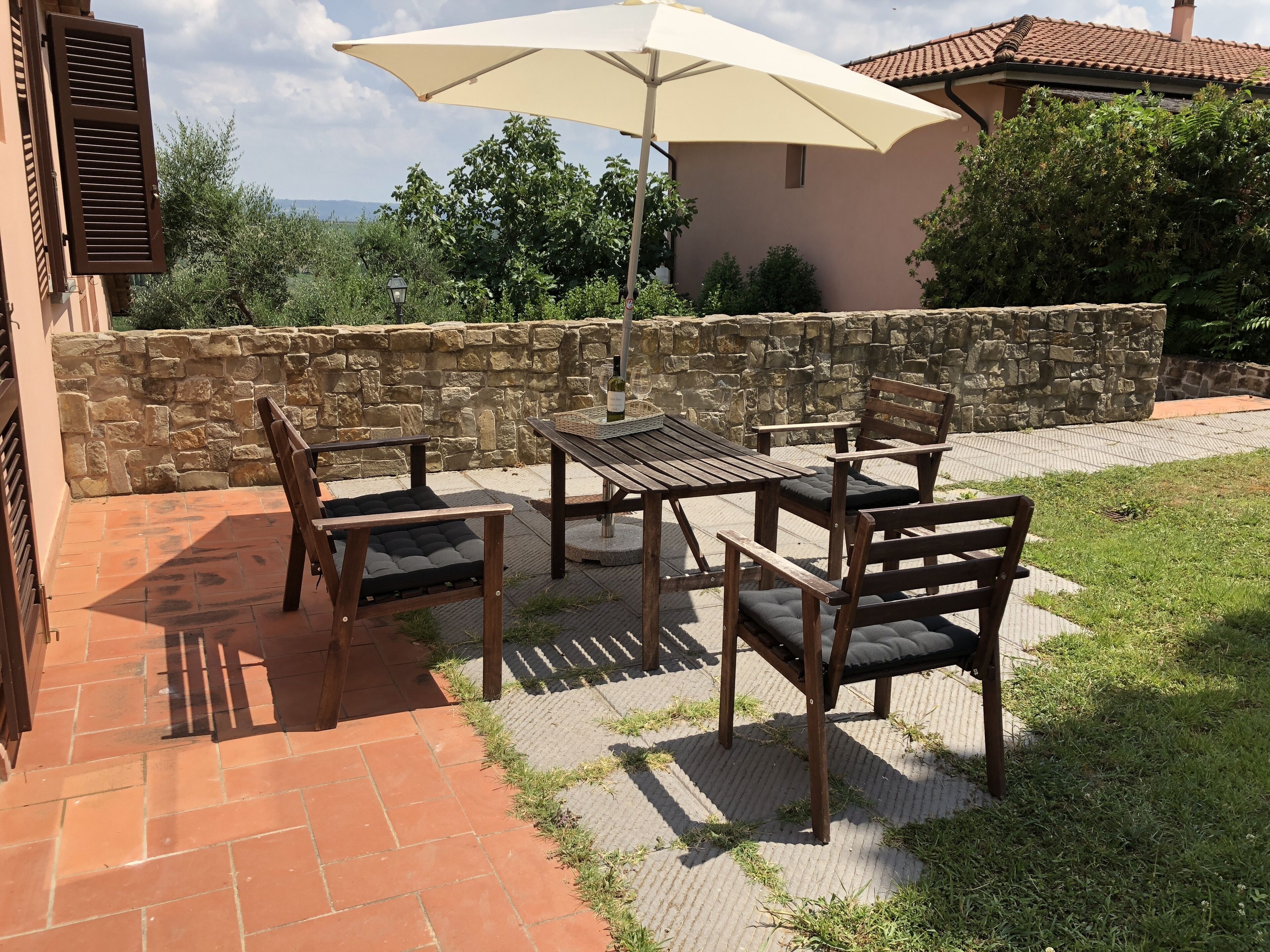 Un patio al aire libre con pared de piedra, mesa de madera y sillas.