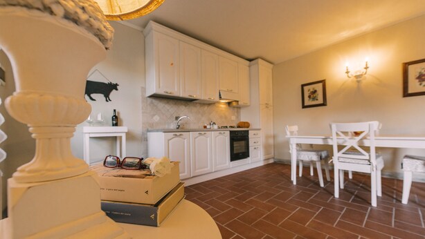 Une cuisine avec des meubles blancs, une table à manger avec des chaises et un sol carrelé.