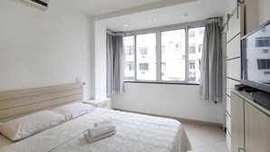 Ein Hotelzimmer mit einem großen Bett, einem Fernseher, einem Kleiderschrank und einem Fenster mit Vorhängen.