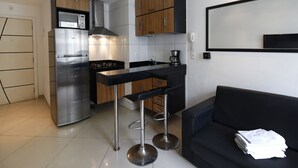 Eine kompakte Küche mit Kühlschrank, Mikrowelle und Herd, neben einem schwarzen Sofa und einer kleinen Bar mit Barhocker.