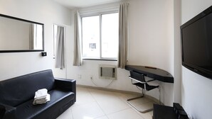 Ein Hotelzimmer mit schwarzem Ledersofa, einem Flachbildfernseher, einem Schreibtisch mit Stuhl und einem großen Fenster mit Vorhängen.
