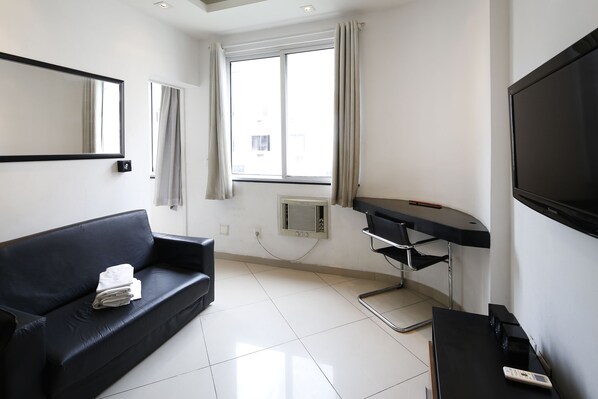 A hotel room with a black leather sofa, a flat-screen TV, a desk with a chair, and a large window with curtains. - Rio Rentals 021 - U010 Excelente apartamento em Copacabana (Rio de Janeiro)