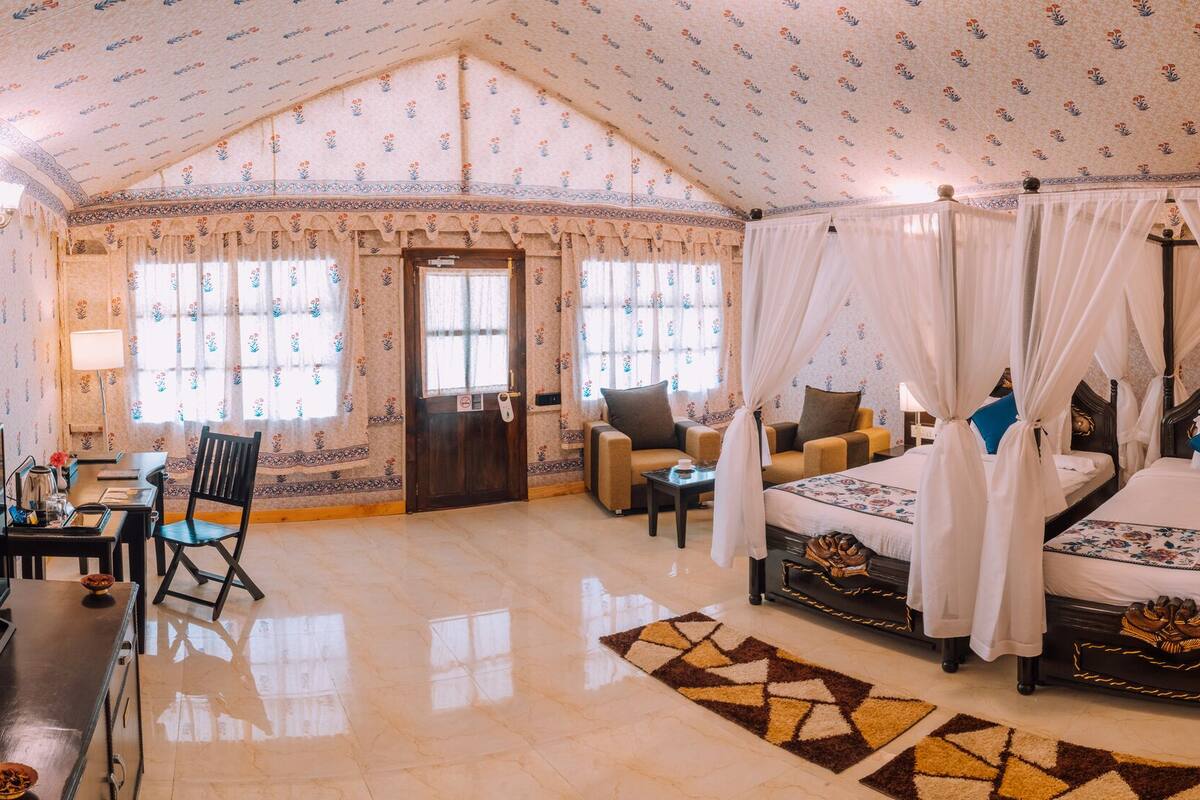 A room with a bed, a desk, and a chair. There is a window with curtains and a clock on the wall.