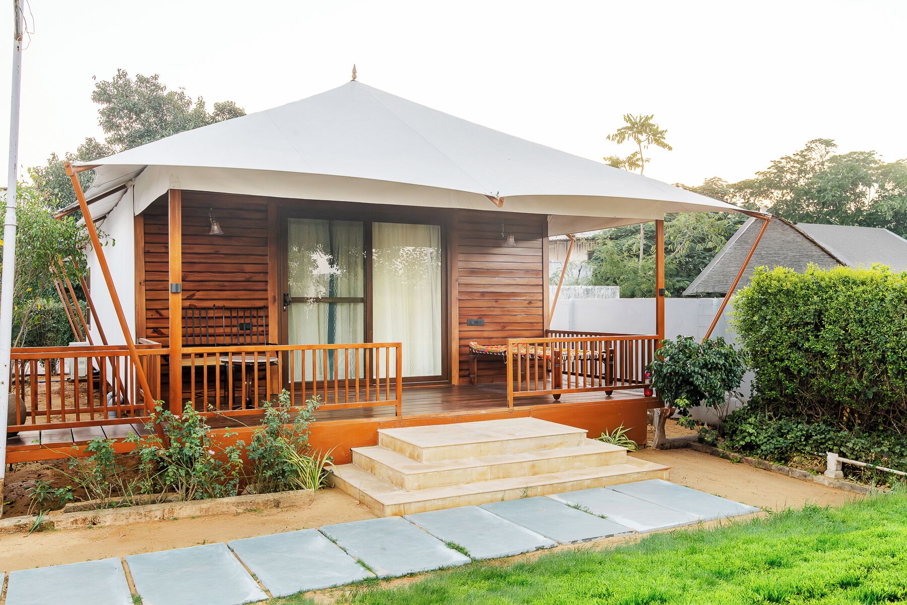 A wooden house with a covered porch, steps leading to the entrance, and a garden area.