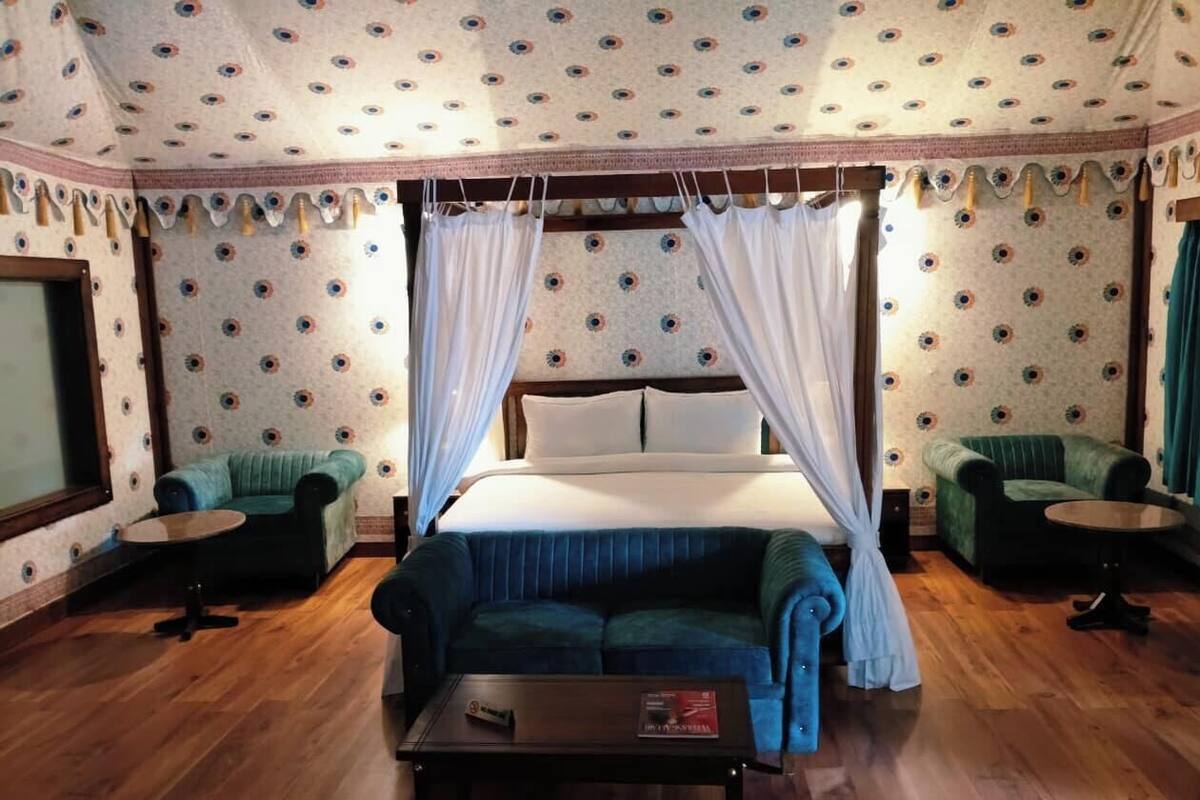 A room with a bed, two armchairs, a small table, and a canopy bed.