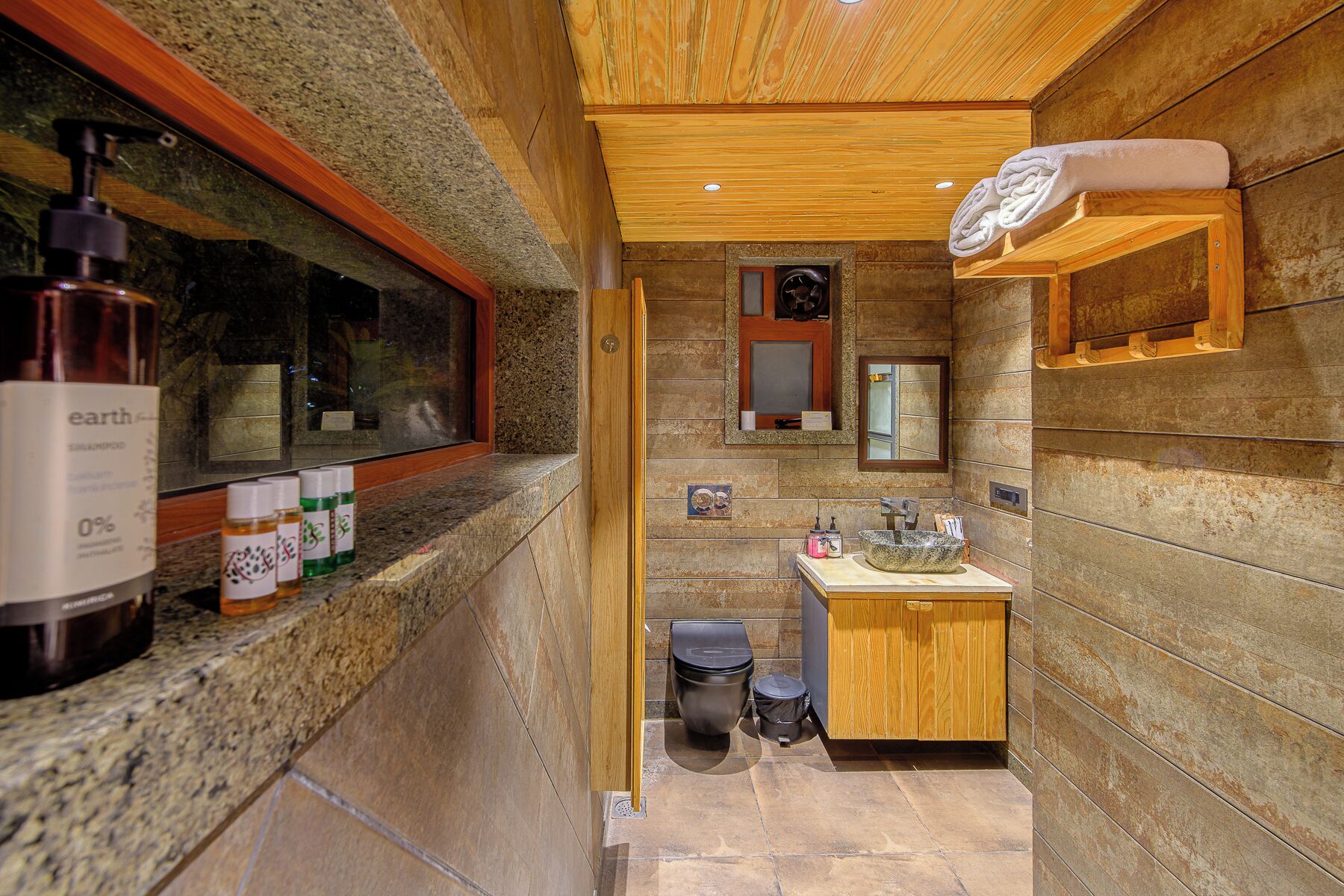 A bathroom with a wooden vanity, a sink, and a toilet. There are toiletries on the counter.