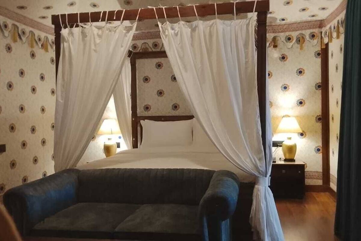 A four-poster bed with white drapes, a blue sofa, and two bedside lamps.