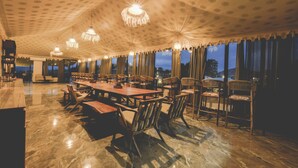 Un comedor espacioso con una larga mesa de madera y sillas, techo con diseño y ventanas grandes con cortinas.