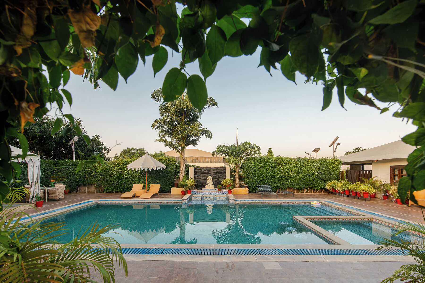 A swimming pool with lounge chairs, a stone wall, and potted plants.