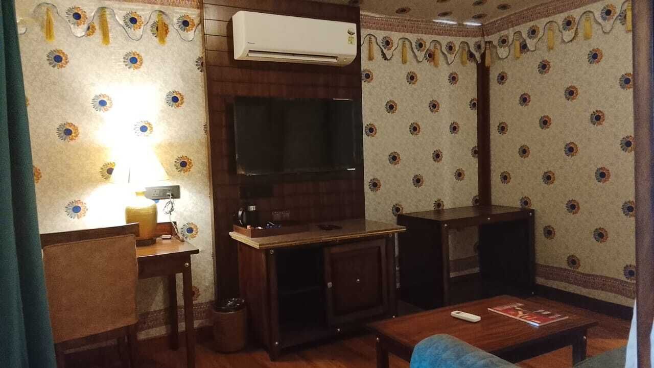 A living room with a TV, wooden furniture, and patterned wallpaper.