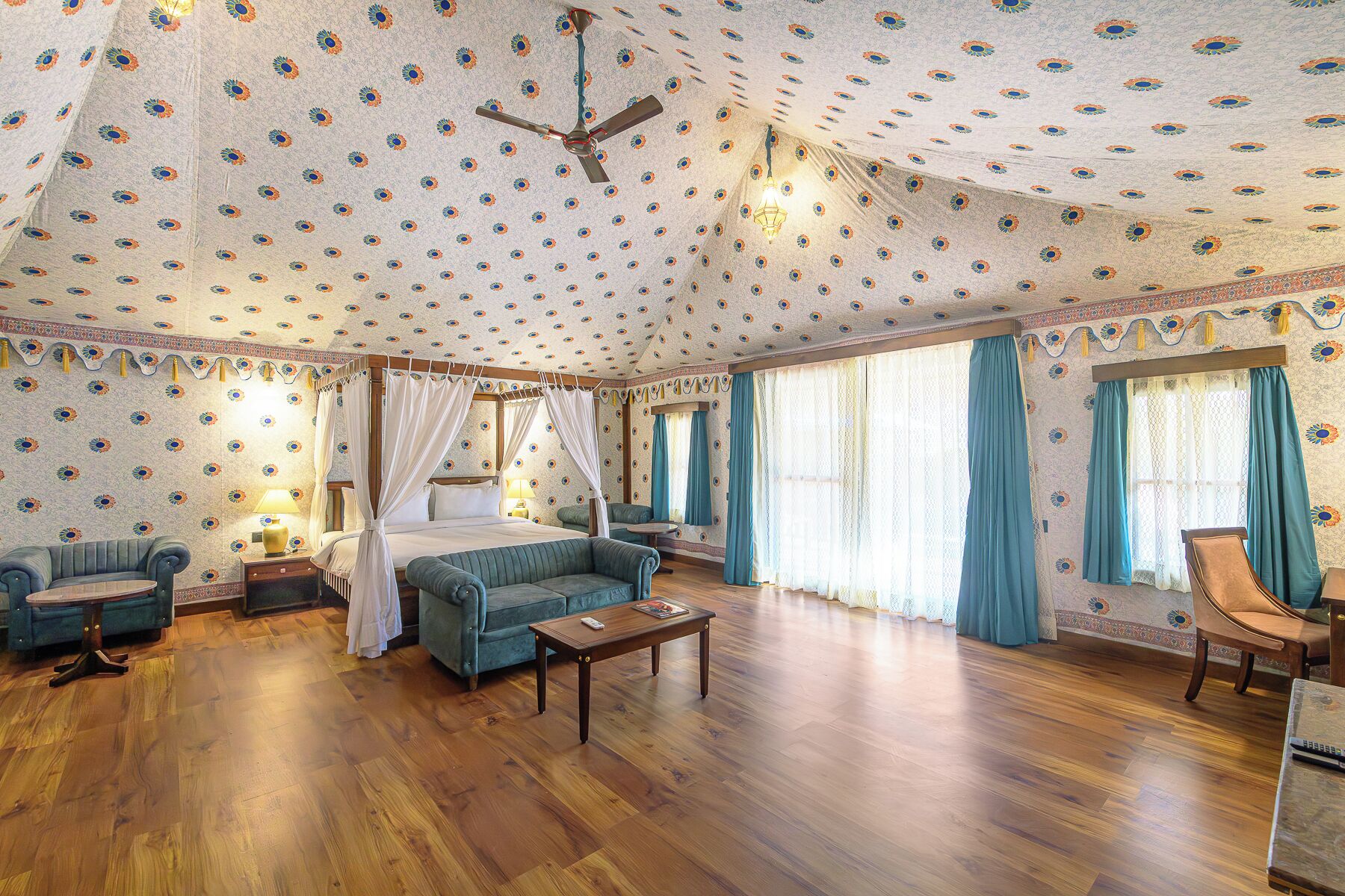 Ein Zimmer mit einem Bett, zwei Sofas, einem Tisch, einem Deckenventilator und Wandtapete mit Muster.