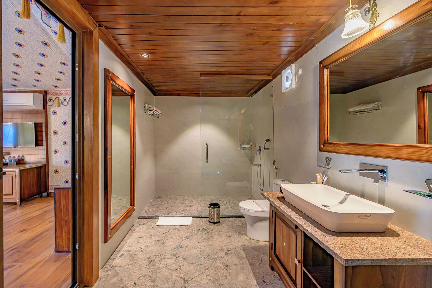 Baño con ducha, inodoro y lavamanos, techo de madera y espejos amplios.