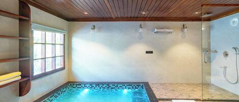 A spa room with a hot tub, a glass shower enclosure, and a window with blinds.