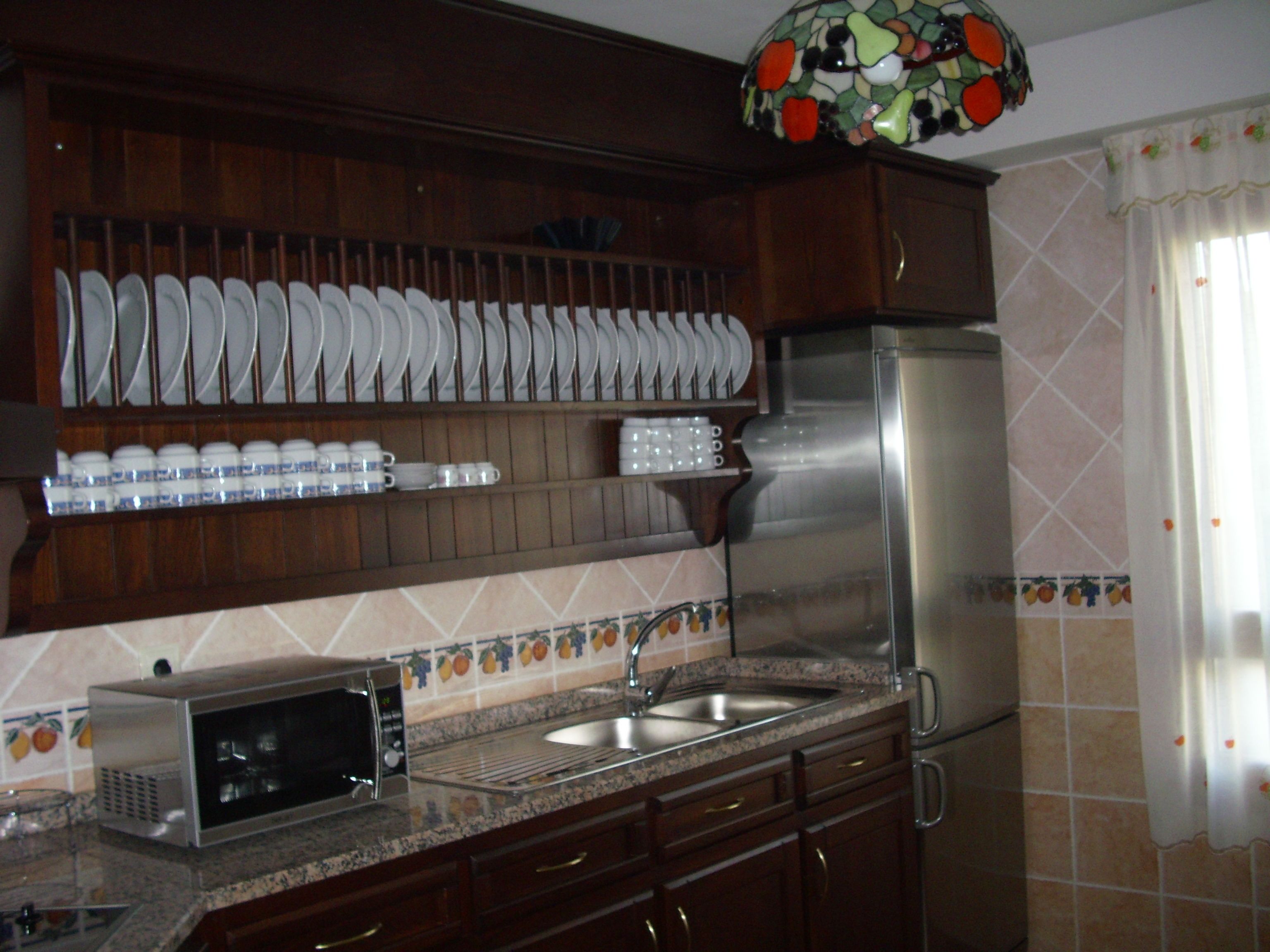 Una cocina con gabinetes de madera, un refrigerador de acero inoxidable, un microondas y un fregadero.
