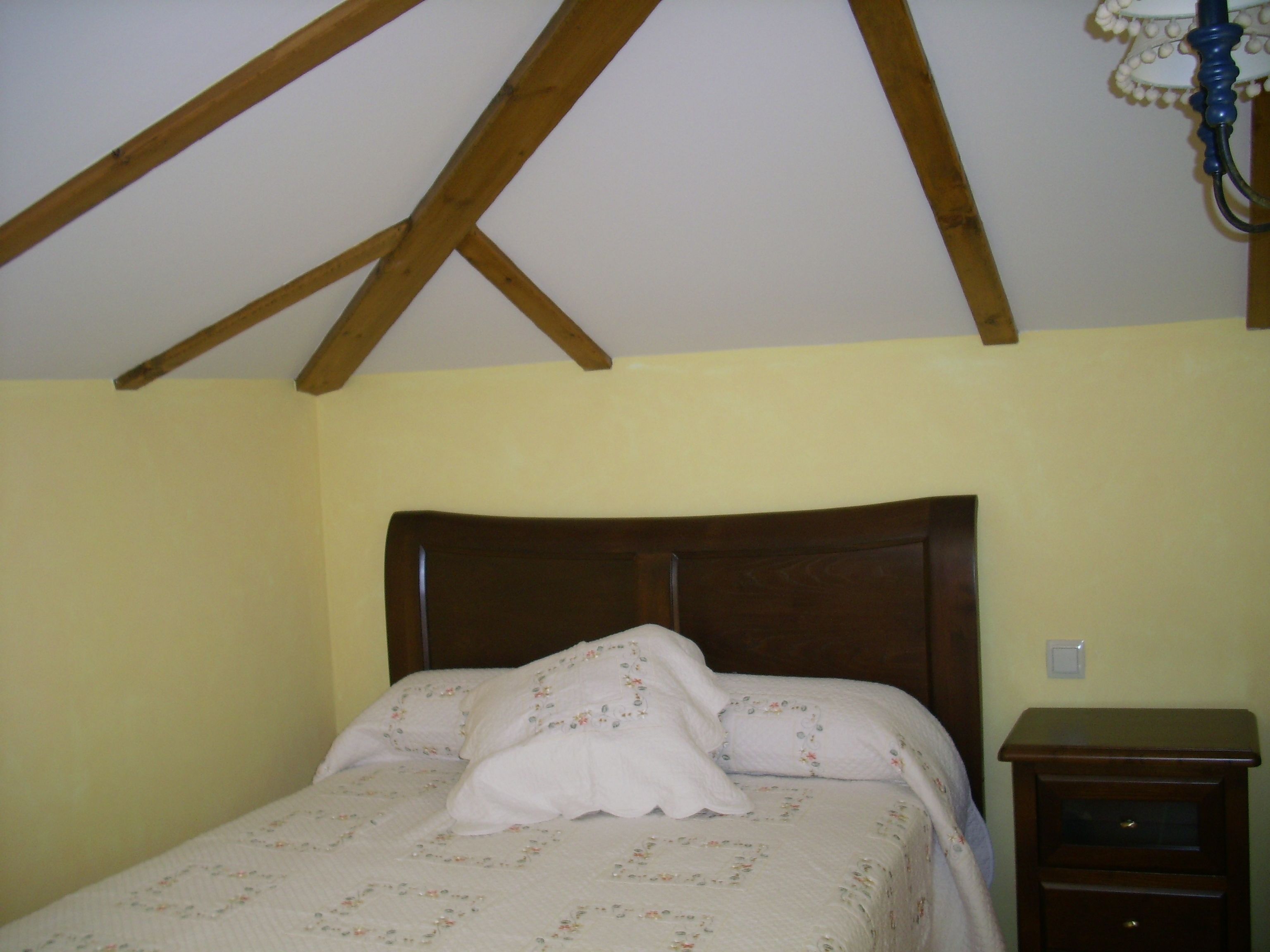 A bedroom with a wooden ceiling, a bed with floral bedding, and a nightstand.