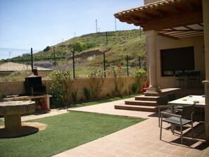 An outdoor patio with a grill, seating area, and a view of a hilly landscape. - Casa Rural Las Murallas (Brihuega)