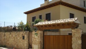 A two-story building with a tiled roof, a stone wall, and a wooden gate. - Casa Rural Las Murallas (Brihuega)