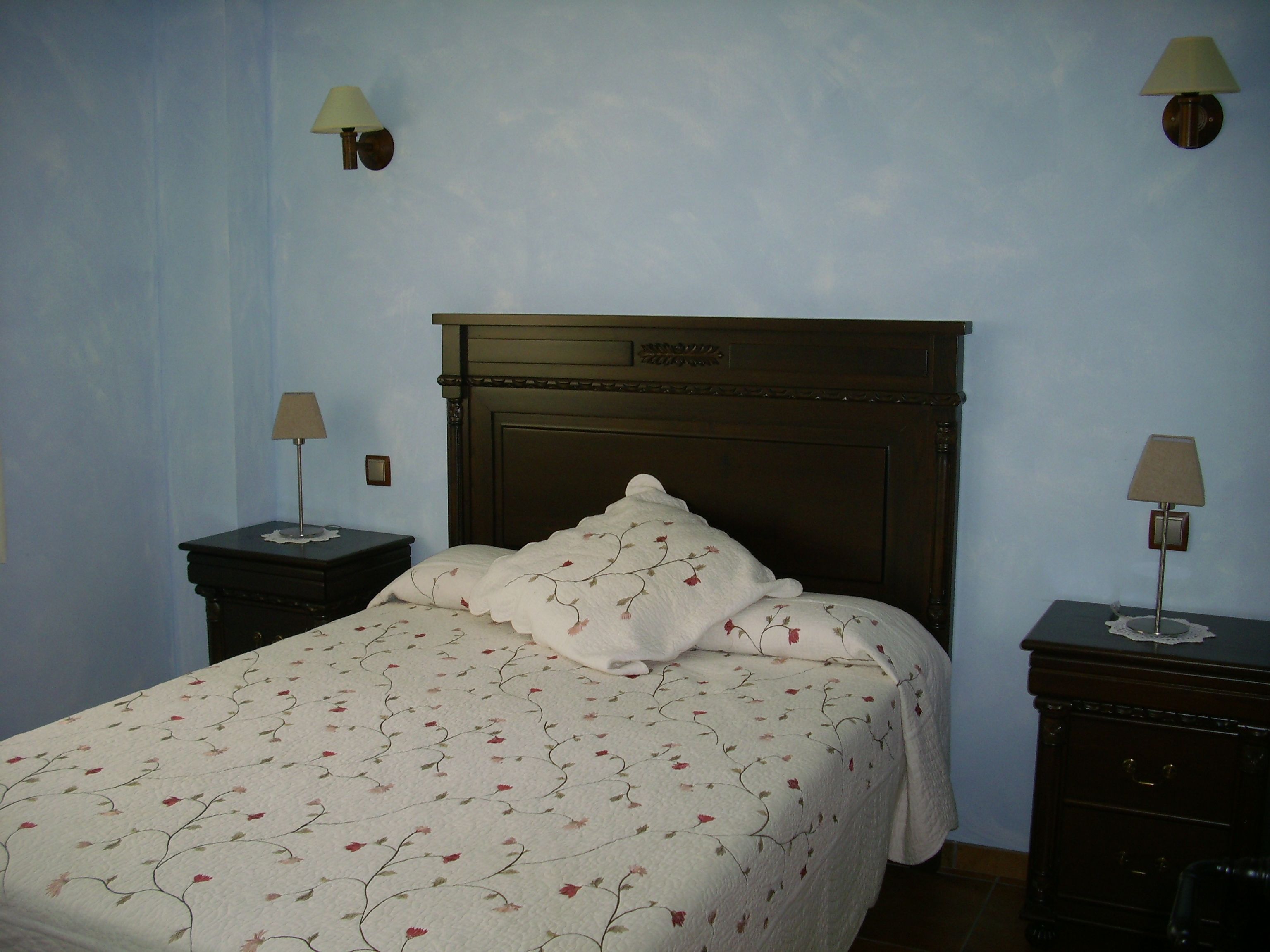 Un dormitorio con una cama, dos mesitas de noche y dos lámparas de pared.