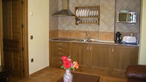 A kitchen with wooden cabinets, a microwave, a toaster, and a vase with flowers on a table. - Casa Rural Las Murallas (Brihuega)