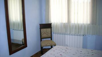 Un dormitorio con cama, una silla, un radiador y una ventana con cortinas.